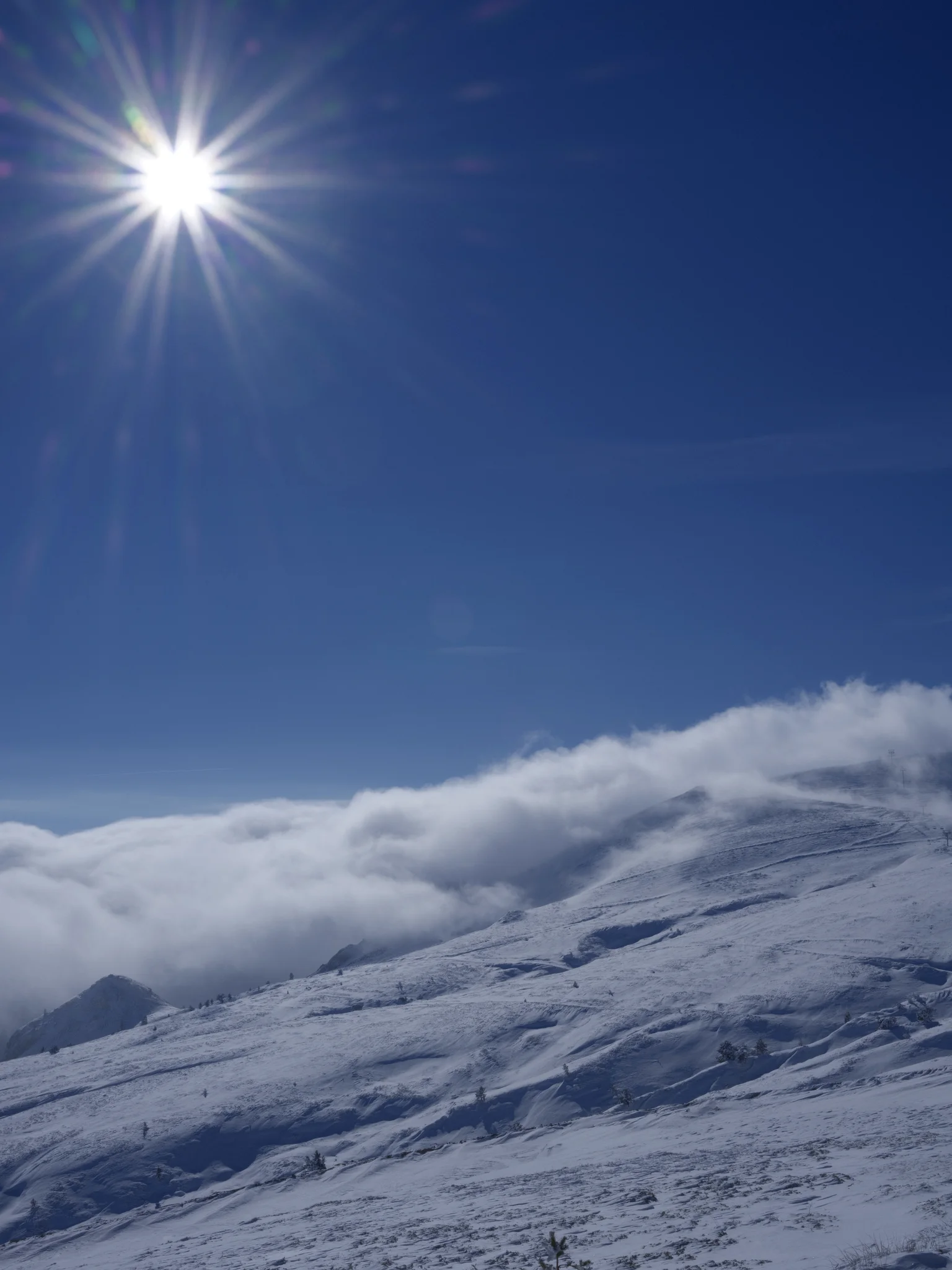 Schneebedeckter Grat über einem Wolkenmeer; Sonne als Stern mit f/32.
